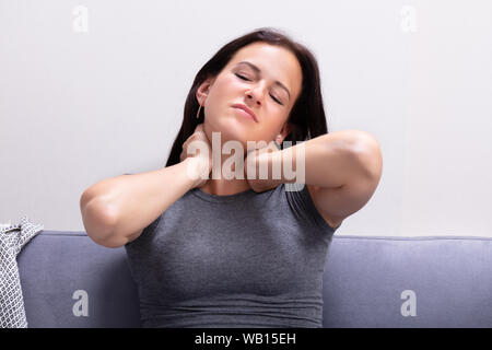 Ritratto di giovane donna che soffre di dolori al collo a casa Foto Stock
