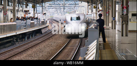 Il il treno superveloce Shinkansen di Hakata arriva alla Stazione di Kanazawa mentre una guardia o treno ufficiale del servizio attende. Foto Stock