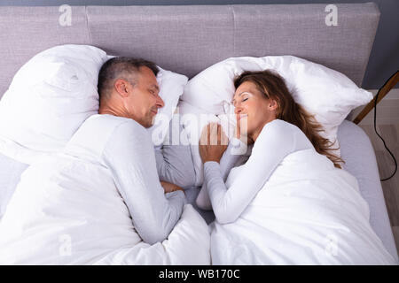 Angolo di Alta Vista della Coppia Matura che dorme sul letto di casa Foto Stock