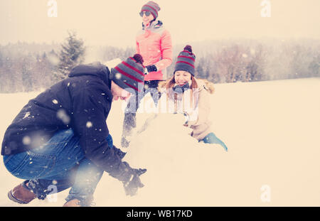 Gruppo di giovani happy business persone aventi un concorso nella realizzazione di pupazzi di neve mentre godendo nevoso inverno giornata con i fiocchi di neve attorno a loro nel corso di un team Foto Stock