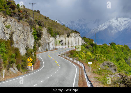 Nuova Zelanda, Isola del Sud, strada tortuosa in orizzontale lungo il lago Hawea con il Sud delle Alpi in background Foto Stock