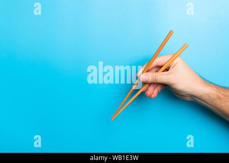 Immagine creativa delle bacchette di legno nelle mani di sesso maschile su sfondo blu. Il giapponese e il cinese del cibo con copia spazio. Foto Stock
