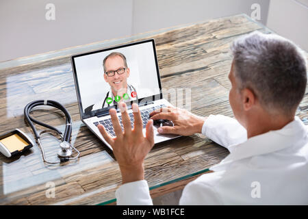 Close-up di medico avente Video Conferenza su laptop alla scrivania in legno Foto Stock