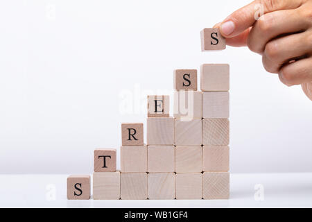 Persona della mano che trattiene i blocchi di legno ponendo ultimo alfabeto della parola Stress sulla scrivania bianca Foto Stock