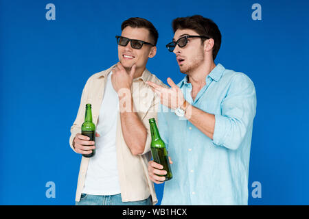 Due amici di occhiali 3d azienda di bottiglie di birra isolato su blu Foto Stock