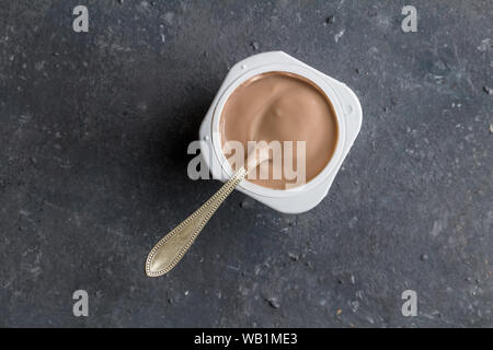 Cioccolato yogurt aromatizzati in una tazza di plastica con il cucchiaio sul grigio Sfondo texture - vista superiore foto della tazza di yogurt Foto Stock