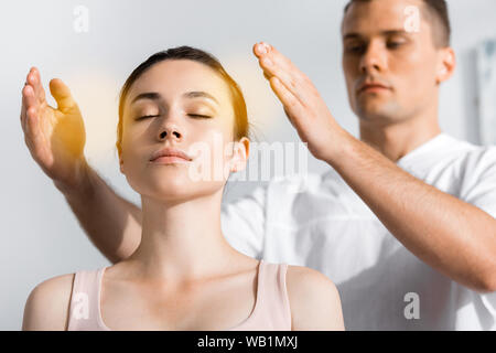 Donna seduta con gli occhi chiusi mentre il guaritore la pulizia la sua aura Foto Stock