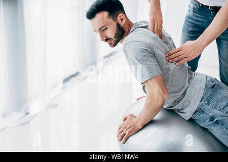 Massaggio chiropratico retro dell uomo bello giacente sulla sfera di fitness Foto Stock