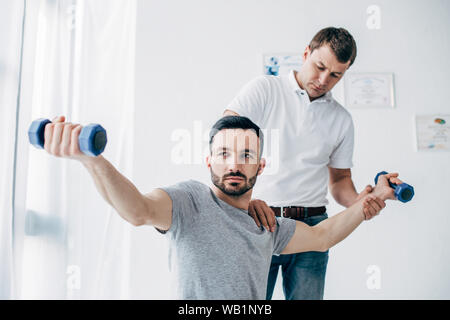 Chiropratico stretching braccio del paziente bello con manubri in ospedale Foto Stock