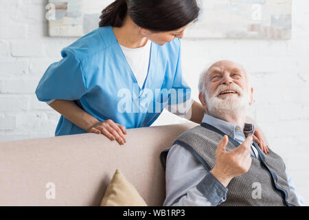 Felice l'uomo senior guardando un infermiere, seduto sul lettino Foto Stock