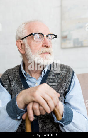 Calma e triste senior uomo con bastone che guarda lontano, seduti nella sala luminosa Foto Stock