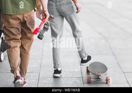Vista ritagliata di un uomo e di una donna che cammina sulla strada con skateboard Foto Stock