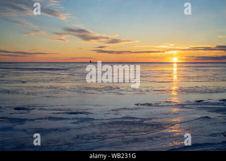 Il sole che tramonta su un porto congelati nelle zone rurali di Prince Edward Island, Canada. Faro all'orizzonte. Foto Stock