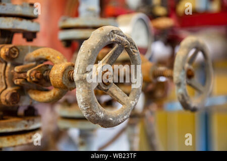 Condutture industriali e le valvole si chiudono, la sfocatura dello sfondo. Vecchio arrugginito apparecchiature di controllo, abbandonata impiantistica industriale Foto Stock