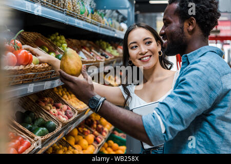 Felice donna asiatica guardando african american man nei pressi di frutti in negozio Foto Stock