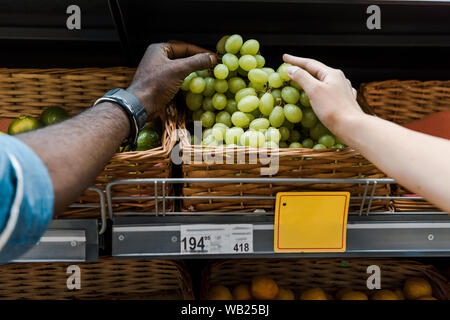 Vista ritagliata della americano africano l uomo e la donna prendendo le uve in store Foto Stock