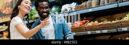 Panoramica di felice ragazza asiatica puntando con il dito nelle vicinanze African American uomo in negozio Foto Stock