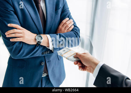 Vista ritagliata dell'uomo dando denaro contante al business partner in piedi con le braccia conserte su bianco Foto Stock