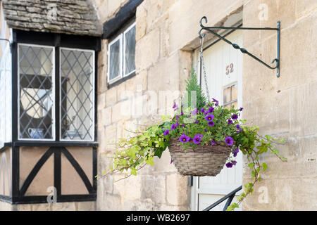 Fiori di petunia in una cesta appesa di fronte a una pietra di Cotswold House di Winchcombe, Cotswolds, Gloucestershire, Inghilterra Foto Stock