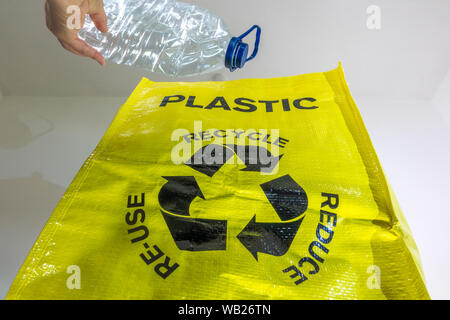 Chiudere shot di una mano di un uomo collocando un vuoto, schiacciata di acqua in bottiglia in un giallo brillante riciclaggio plastica sacco. Foto Stock