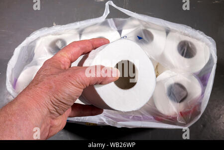 Chiudere POV tettuccio di colpo di un uomo con le mani in mano la rimozione di un bianco fresco la carta igienica da un fornitore multipack. Foto Stock