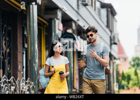 Bel uomo e donna asiatica parlando e tenendo bicchieri di carta Foto Stock