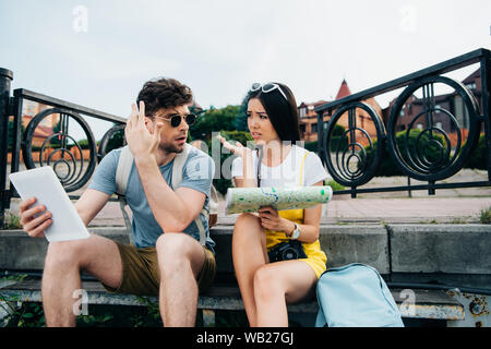 Triste uomo con tavoletta digitale e donna asiatica azienda mappa Foto Stock