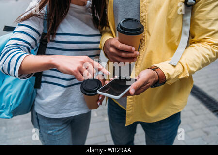 Vista ritagliata della bi-razziale uomo con bicchiere di carta tenendo lo smartphone e donna puntando con il dito Foto Stock