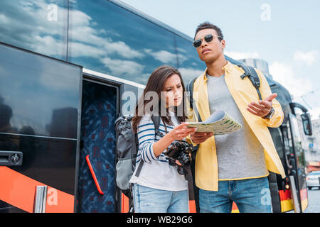 Donna con fotocamera digitale fino sulla mappa di razza mista uomo vicino al bus di viaggio Foto Stock