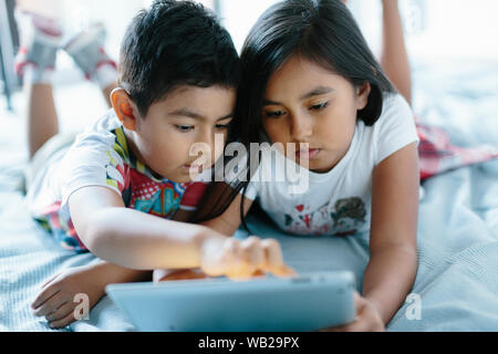 A 9 anno vecchia ragazza e a 5 anno vecchio ragazzo sono sdraiato sul pavimento. Si sta cercando un tablet. Sono vestite con abiti estivi. Si tratta di ore diurne. Essi ha Foto Stock