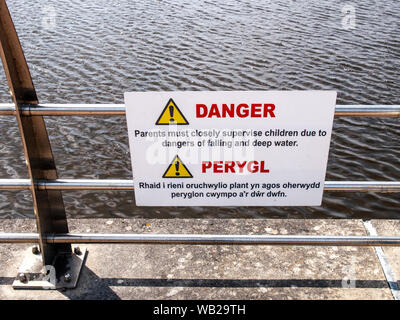 Segnale di avviso circa i pericoli di caduta e di acque profonde a lato del fiume Tawe a Swansea. Doppia lingua. Welsh/inglese. Il Galles, UK. Foto Stock