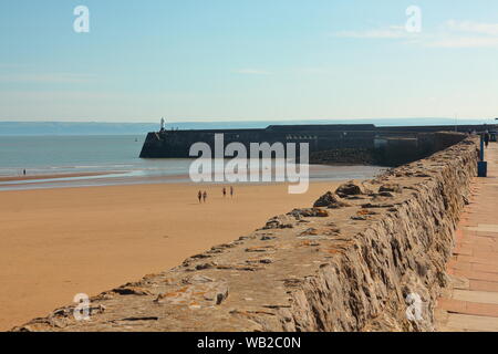 Guardando lungo la promenade parete verso il faro alla fine del molo di attracco delle navi di avvertimento dei pericoli dietro questa splendida spiaggia. Foto Stock