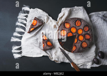 Gustose prugne crostata con cioccolato e due fette su una cucina bianca asciugamano, su una tavola nera. Al di sopra di vista di autunno sweet food. Piatto di laici cadono dessert. Foto Stock