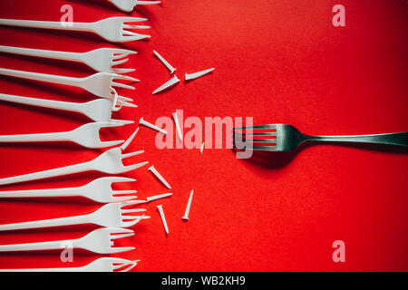 Un sacco di plastica rotta forche vs uno in metallo su sfondo rosso. Il concetto di problemi ambientali, inquinamento ambientale da rifiuti in plastica. Foto Stock