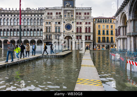 La Torre dell'Orologio (Piazza San Marco Itinerari Segreti di Palazzo Ducale) da una piattaforma sopraelevata durante un'acqua alta alta (acqua), eventi di Piazza San Marco, Venezia, Italia Foto Stock