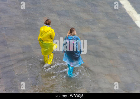 Due donne che indossano soprascarpe impermeabile a piedi attraverso acqua di inondazione durante un'acqua alta (l'acqua alta) evento, la Piazzetta di San Marco, Venezia, Italia Foto Stock
