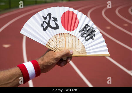 La mano del giapponese sport atleta tenendo una ventola decorate con i caratteri kanji compitazione hisshō, tradotto come vittoria certa, in corrispondenza di una via di corsa Foto Stock