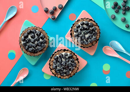 Vista dall'alto su mini mirtillo crema pasticciera torte per bambini festa di compleanno, sano dessert, piatto stendere sui colori rosa e blu della carta. Foto Stock