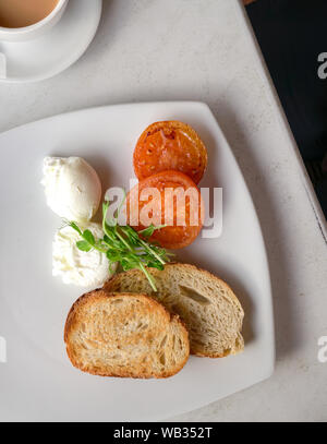 Healhty colazione consiste di uova in camicia, pomodori, pane tostato e verde, con caffè dal lato. Vista dall'alto. Foto Stock
