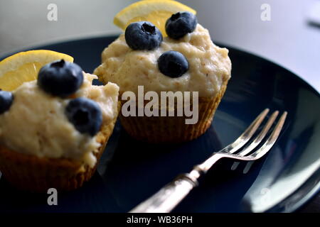 Due cheto crema di limone muffin o tortine con mirtilli servite su blu scuro con piastra forcella d'argento. Closeup, il fuoco selettivo dof poco profondo Foto Stock