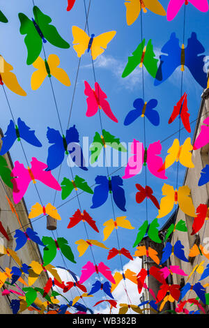 Multi-colorato decorativo in plastica cut-out farfalle al di sopra di una strada pedonale - Chatellerault, Vienne, in Francia. Foto Stock