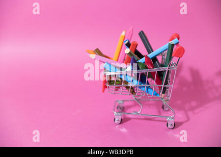 Carrello pieno di penne e matite in cera su sfondo rosa. Istruzione, torna a scuola con il concetto di spazio di copia Foto Stock