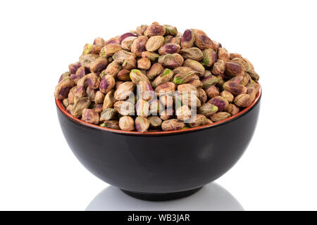 Una ciotola nera piena di pistacchi freschi e sgusciati su sfondo bianco Foto Stock