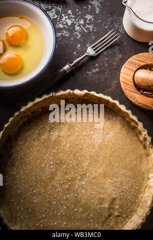 Tart pasta in forma di cottura sul buio tavolo rustico sfondo con utensili da cucina, vista dall'alto. Spazio di copia Foto Stock