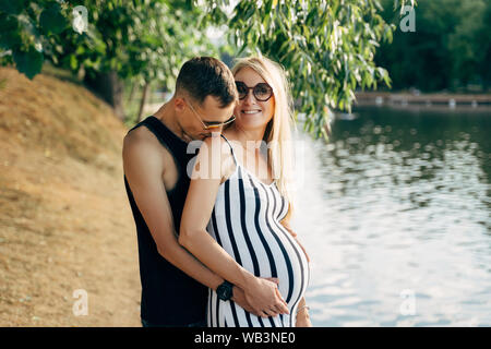 Foto di donne incinta Donna bionda e gli uomini in piedi sulla riva del fiume sul giorno di estate Foto Stock