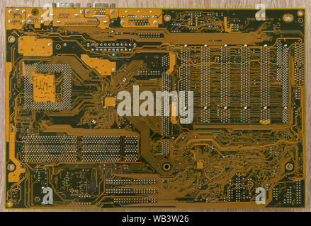 Close-up di una scheda madre per PC su una tavola di legno. Il percorso del circuito. Vista dal basso. Foto Stock