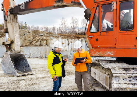 Un uomo e una donna dei lavoratori o dei geologi nei caschi firmare un documento contro lo sfondo di attrezzature da costruzione in una cava Foto Stock