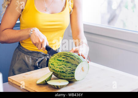 Giovane ragazza bionda il taglio di un melone con un coltello da cucina da una finestra Foto Stock