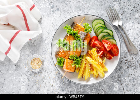 Salmone alla griglia su kebab spiedini con patate al forno, cetrioli freschi e pomodori Foto Stock