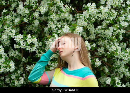 Giovane donna soffre di allergie contro lo sfondo di una ricca fioritura melo Foto Stock
